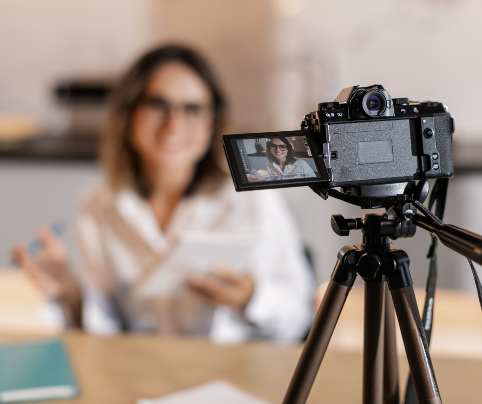 Au premier plan un appareil photo sur un trépied qui filme la personne en arrière plan qui présente un produit.
